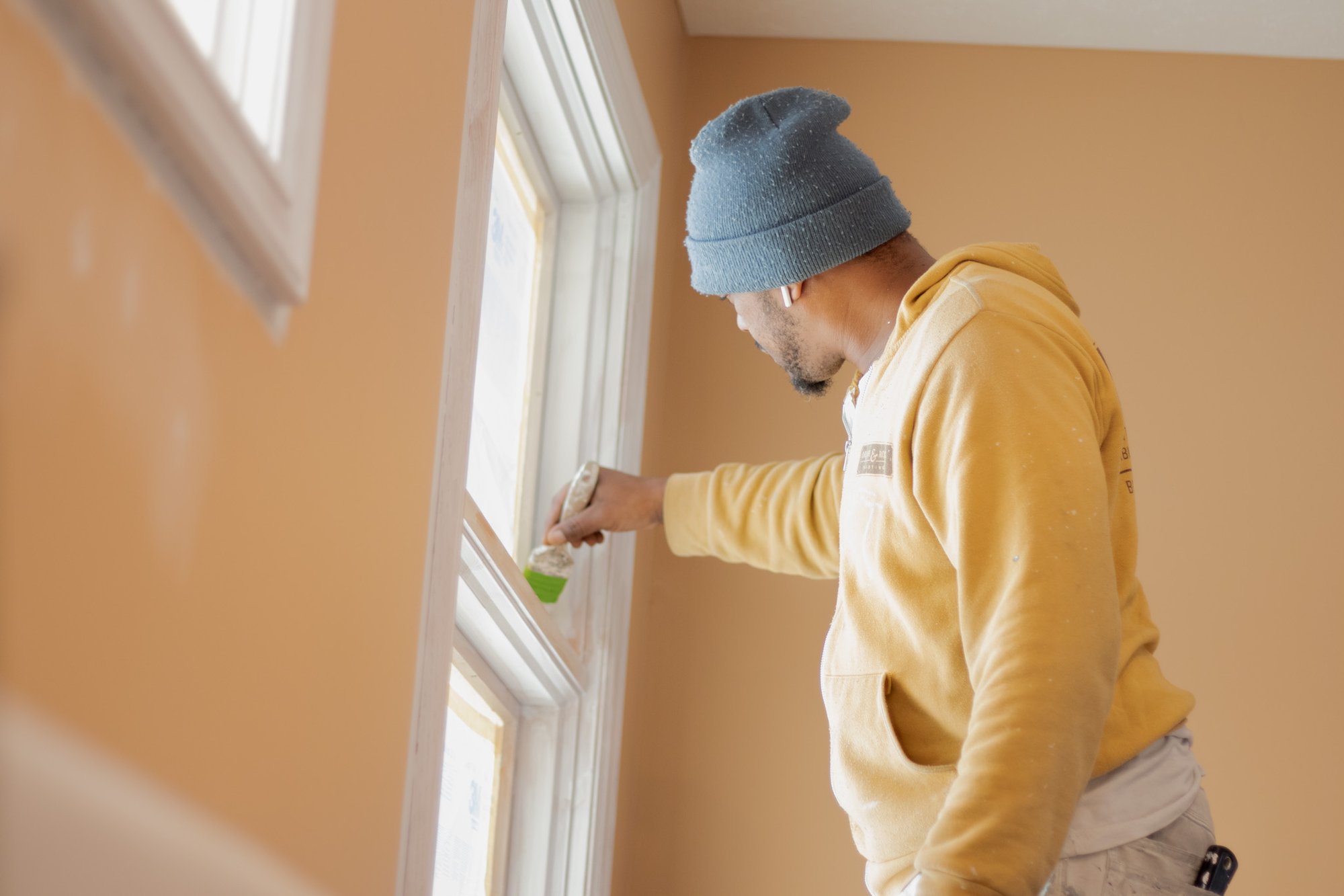 Brush & Roll Painting employee brushing white paint on window trim.