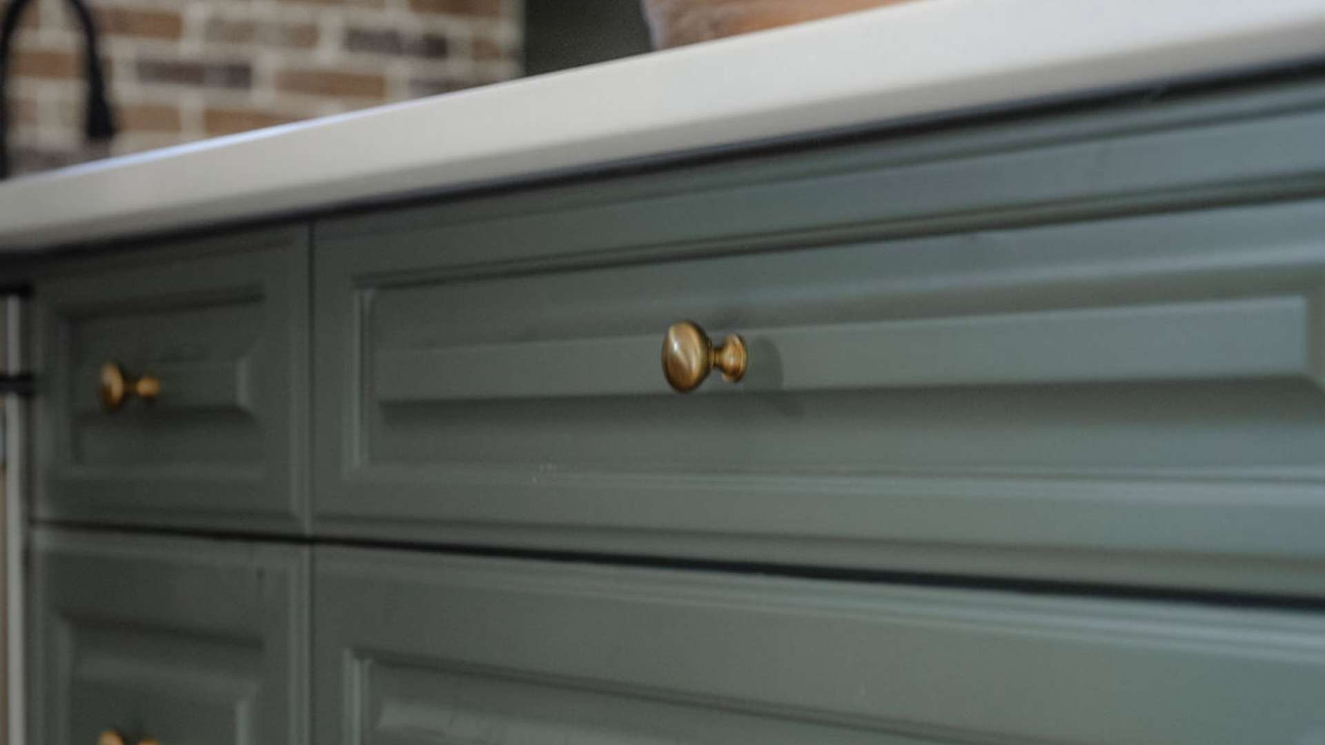 Close up of light green cabinet drawers with gold knobs and white counters on top.