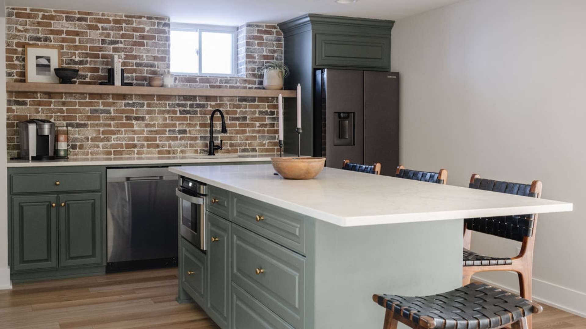 Kitchen with lower sage green cabinets and white countertops, back brick wall and right white wall.