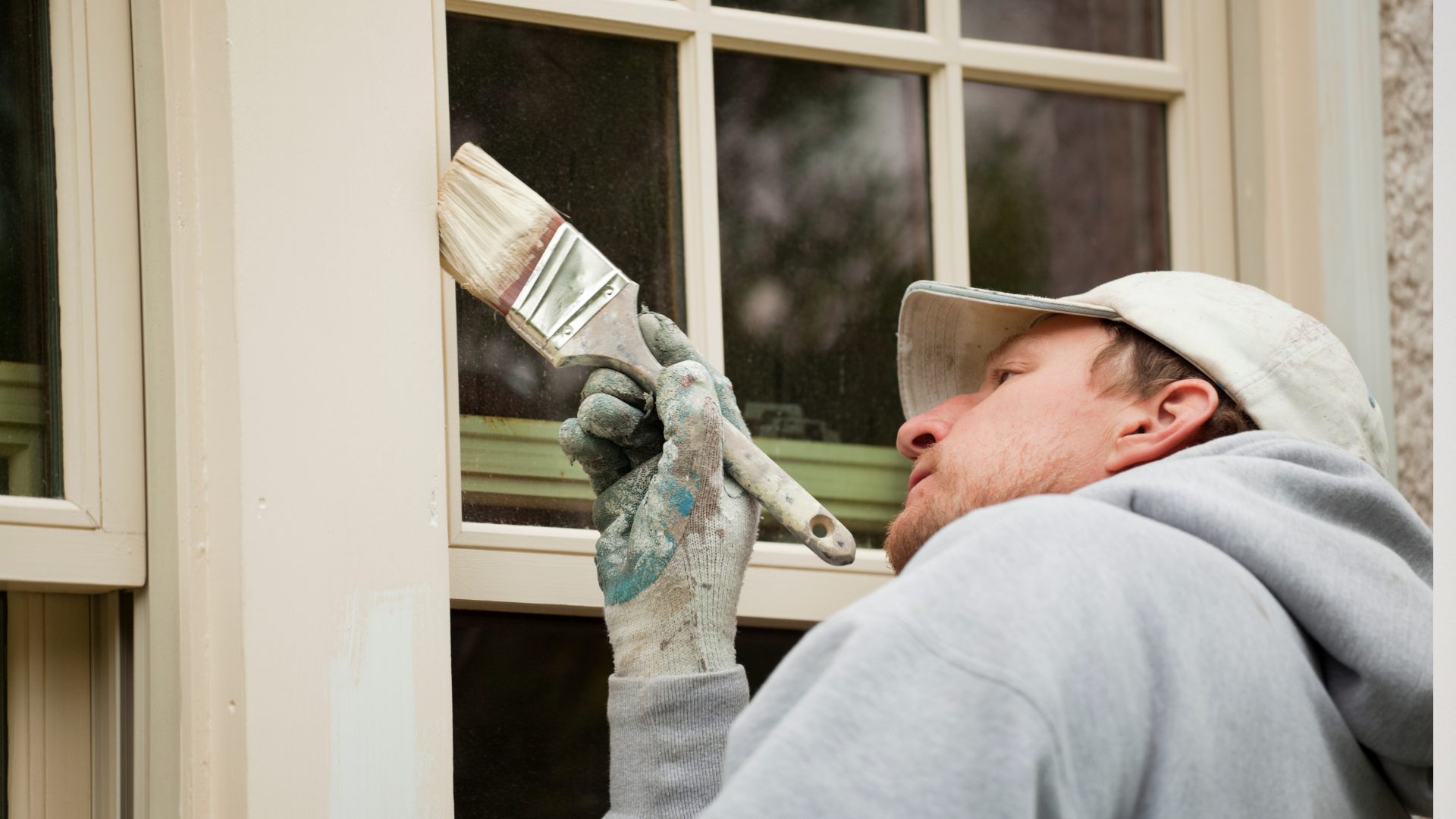 Man touching up exterior windows white paint with brush.